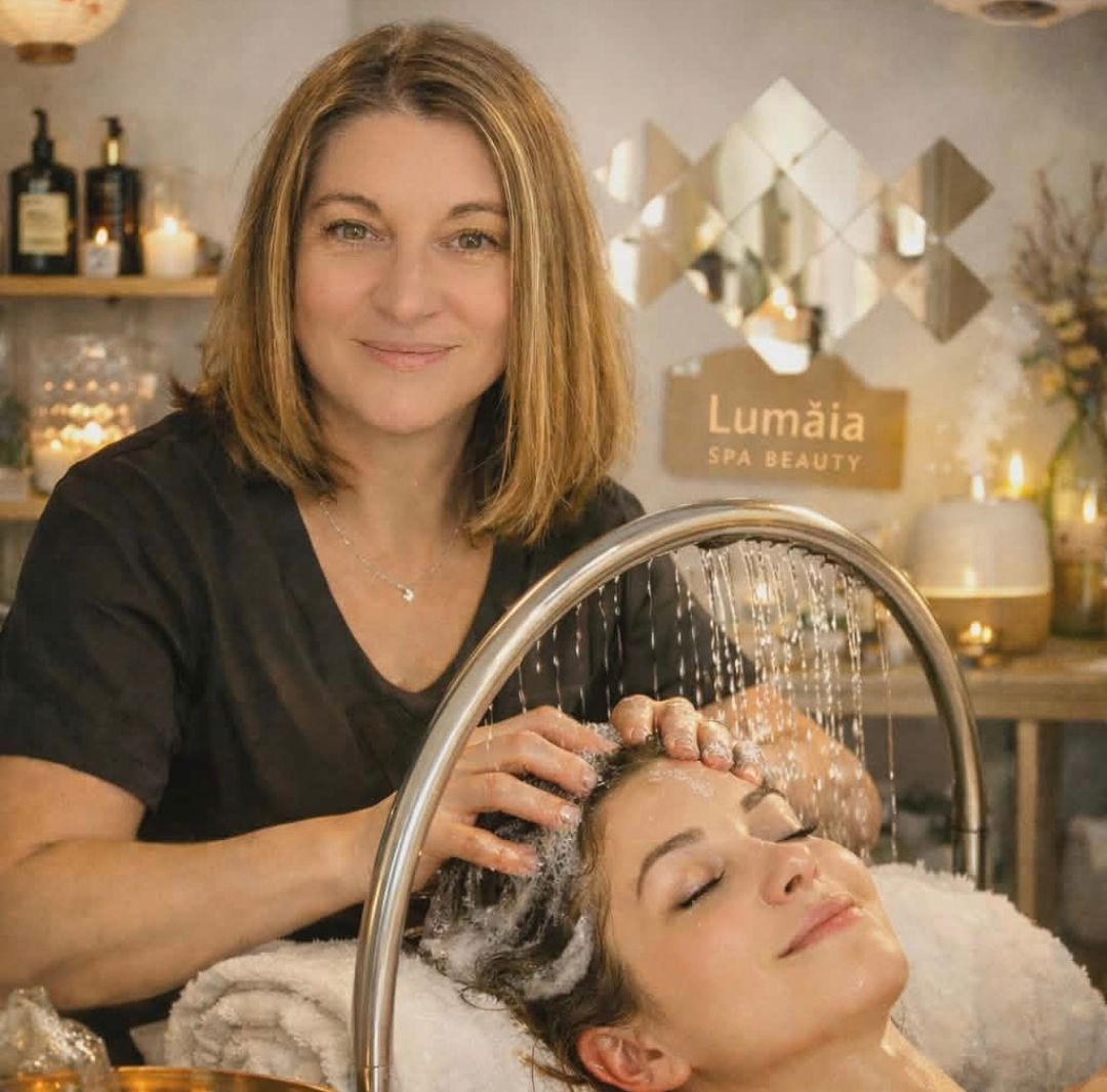 Christelle pendant un head spa, les mains dans les cheveux d'une cliente allongée sous l'arceau de pluie, l'enseigne Lumaïa Spa Beauty au mur